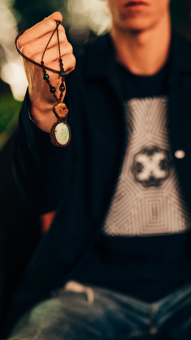 Hand holding a handmade macrame necklace with stone pendants.